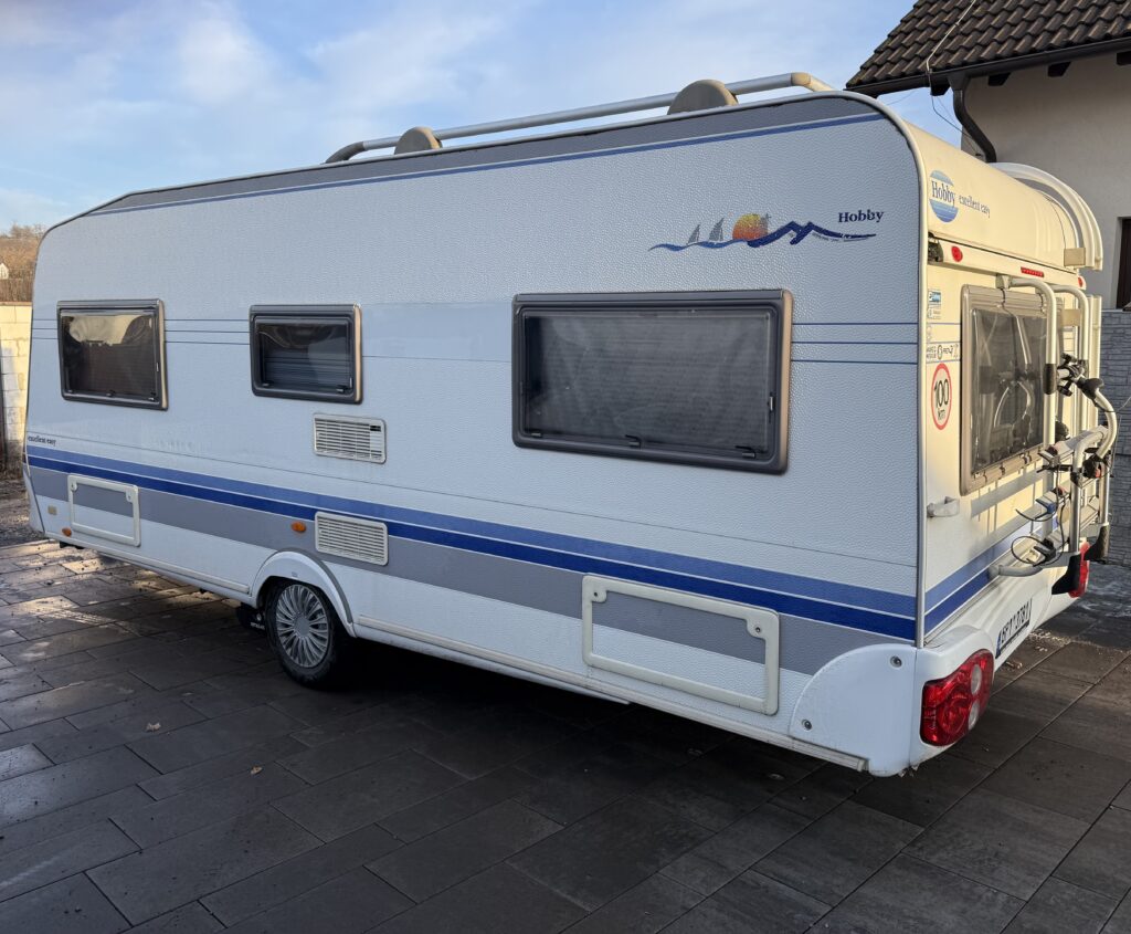 Karavan Hobby s modrými detaily, ideální pro pohodlné cestování a kempování ve volné přírodě.