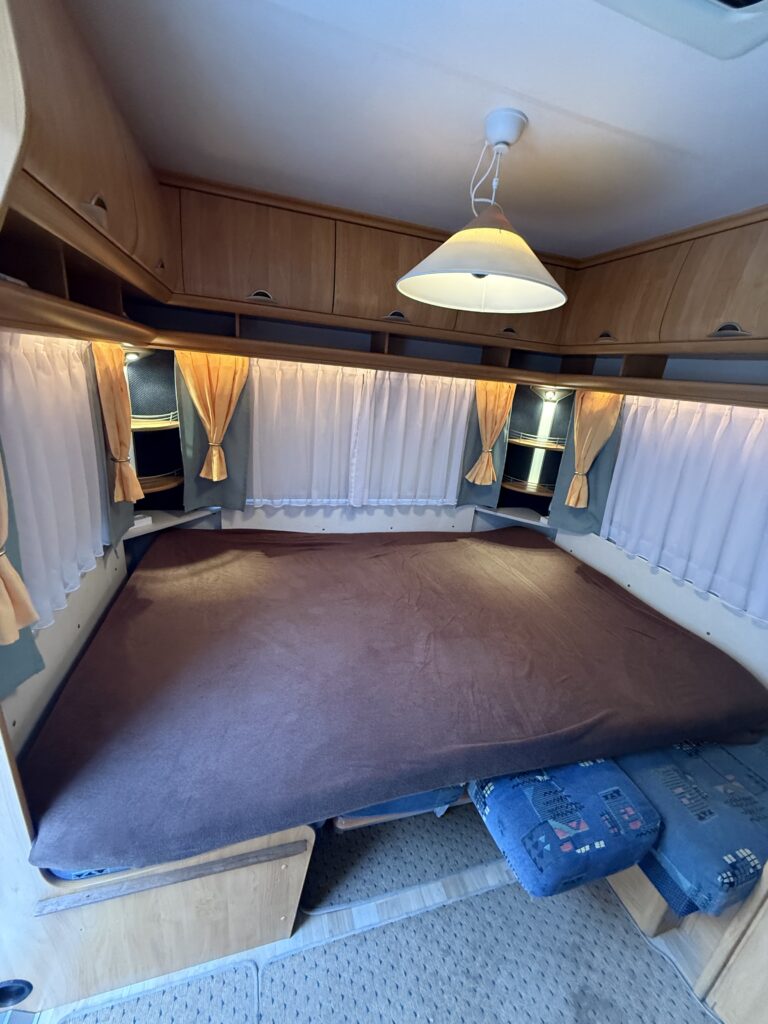 Na obrázku je karavan s prostorným lůžkem a útulným interiérem, ideální pro pohodlné cestování.