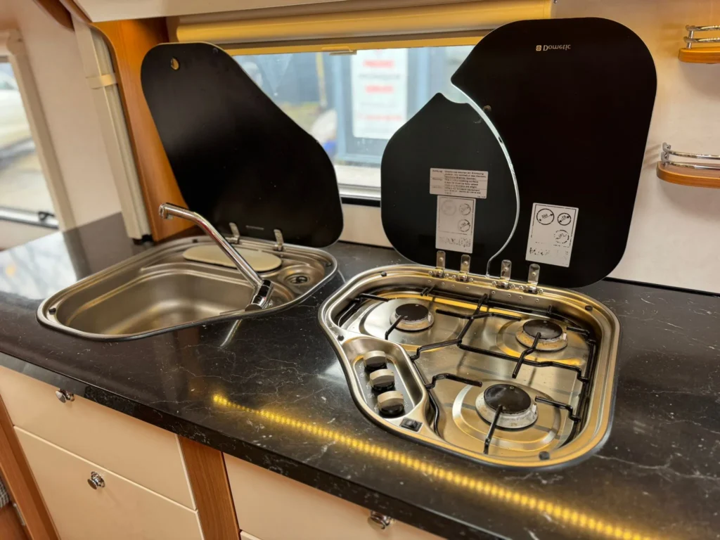 Obrázek z kuchyně obytného vozu s dřezem a sporákem. Vhodné pro pohodlné vaření na cestách.