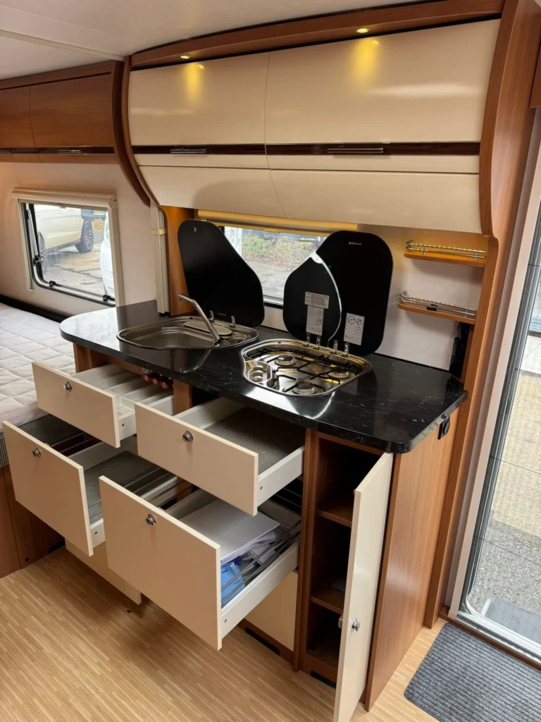 Interiér obytného vozu s moderní kuchyňkou, dřezem a úložnými prostory. Ideální pro cestování a pohodlí.