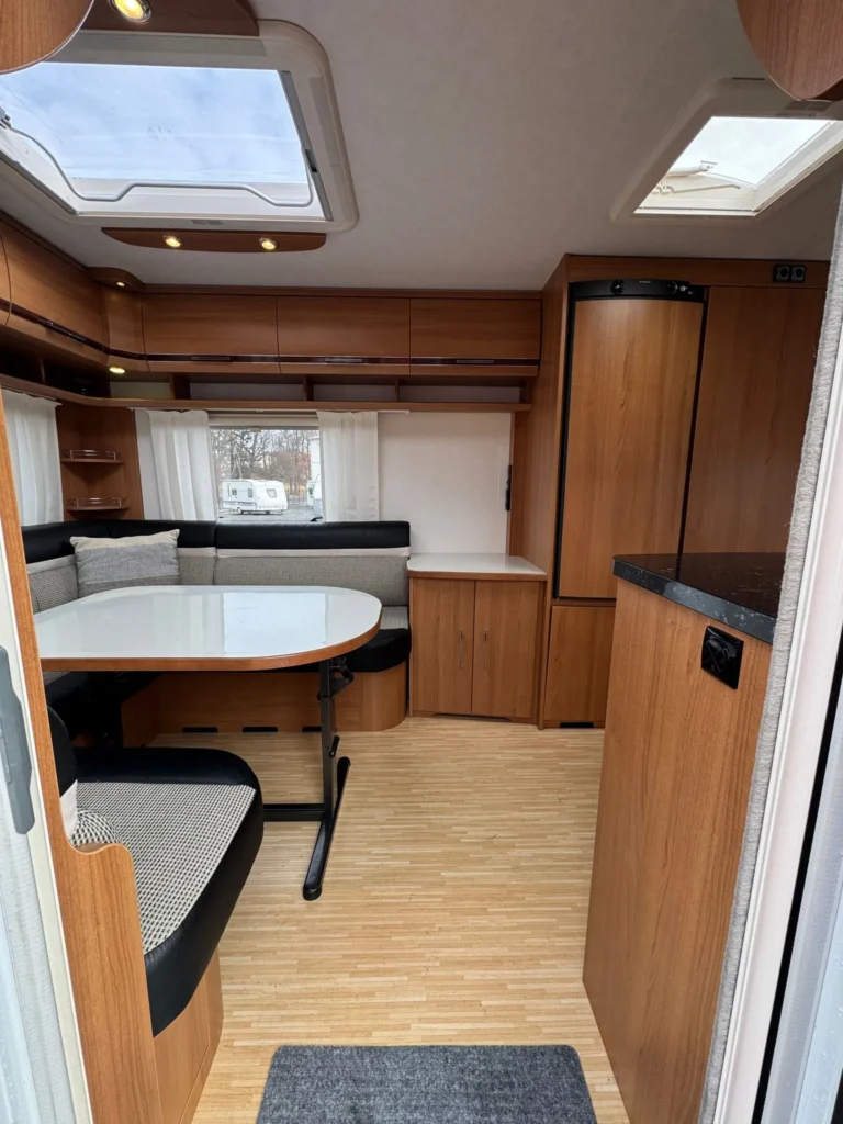 Interiér karavanu s moderním designem, prostorným stolem a pohodlnými sedacími prvky. Ideální pro mobilní dovolenou.