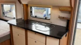 Interiér karavanu s praktickým kuchyňským koutem a úložným prostorem. Elegantní design a moderní vybavení.