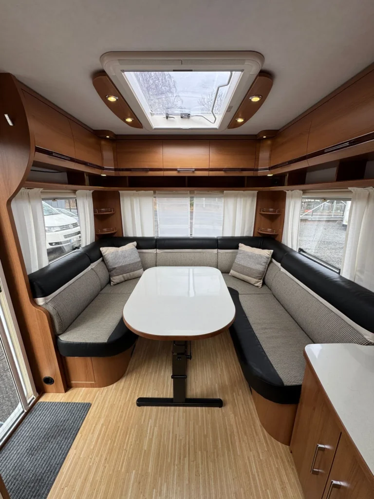 Interiér karavanu s pohodlným sezením a stolem, ideální pro relaxaci a stolování. Elegantní design a čisté linie.