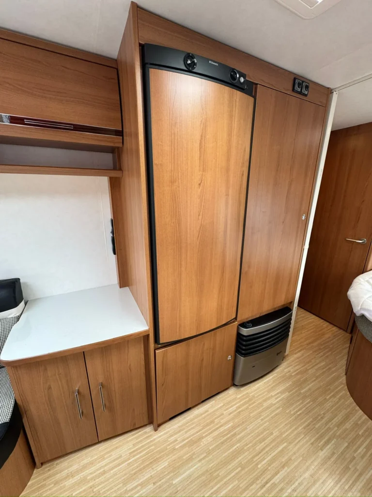 Interiér karavanu s dřevěnými prvky a spotřebiči. Moderní design a praktické uspořádání prostoru na cestování.