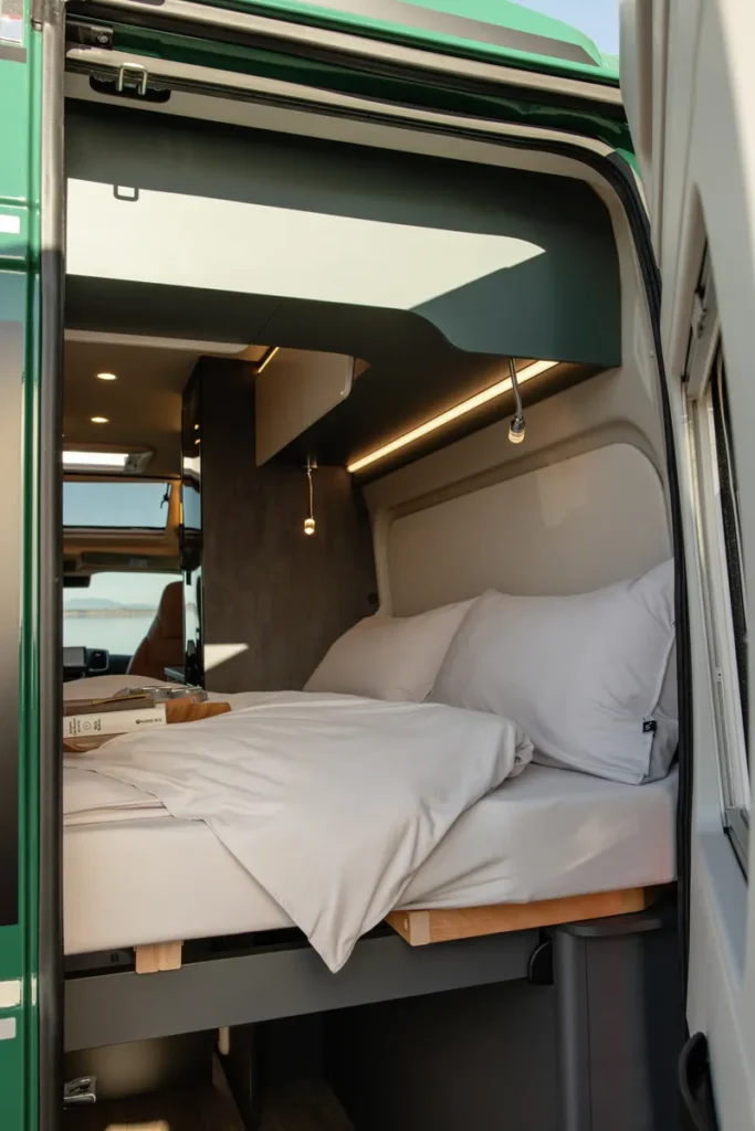 Obrázek ukazuje interiér obytného auta s prostornou postelí a moderním designem.