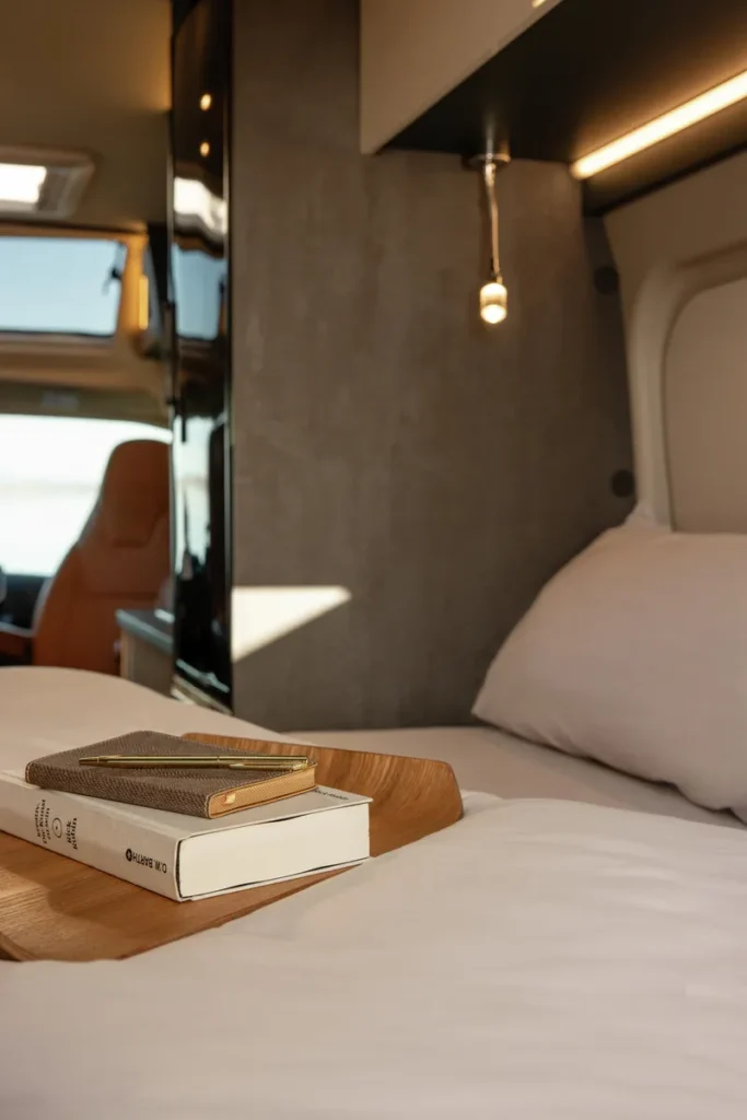 Obrázek interiéru obytného auta s postelí, knihou a zápisníkem. Moderní a útulný design pro pohodlné cestování.