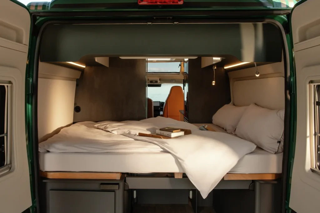 Obrázek ukazuje interiér obytného auta s pohodlnou postelí a moderním designem. Ideální pro cestování.
