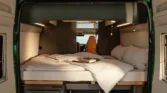 Obrázek ukazuje interiér obytného auta s pohodlnou postelí a moderním designem. Ideální pro cestování.