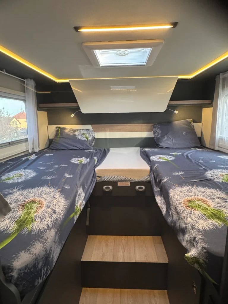 Moderní interiér karavanu s dvojlůžkem a příjemným osvětlením, ideální pro pohodlné cestování.