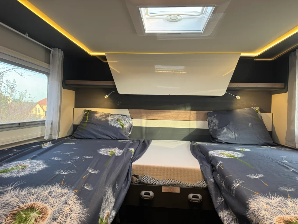 Obrázek ukazuje moderní interiér obytného auta s dvěma jednolůžky a decentním osvětlením.