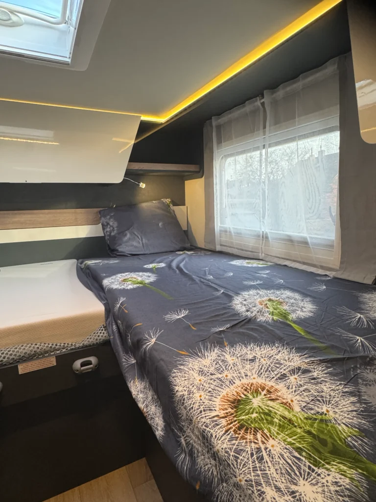 Obrázek zobrazuje útulnou ložnici v obytném autě. Moderní interiér s květinovým motivem.