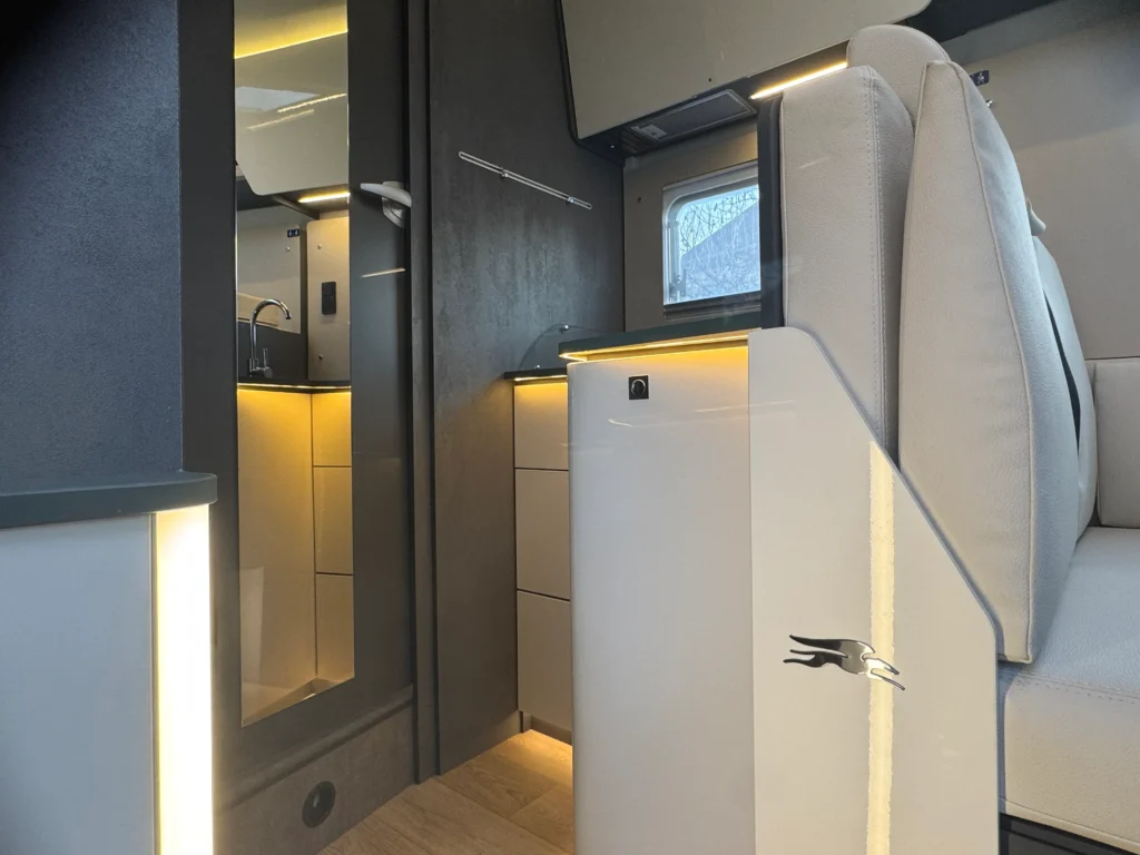 Obrázek zobrazuje interiér moderního obytného auta s elegantním designem a LED osvětlením.