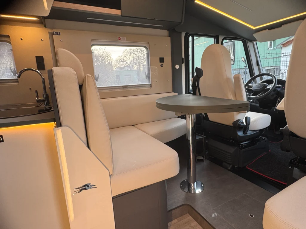 Obrázek interiéru obytného auta, elegantní designe, sezení a stůl, ideální pro kempování.