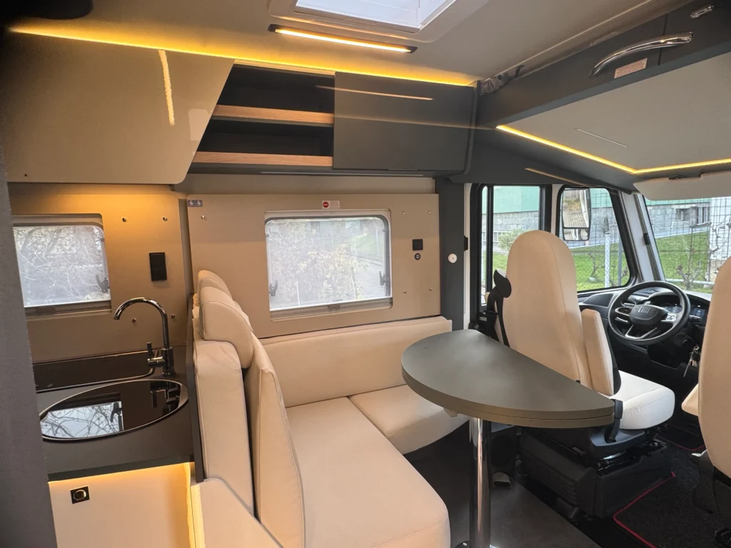 Obrázek interiéru obytného auta, moderní vzhled s kuchyňským koutem a pohodlnými sezeními.