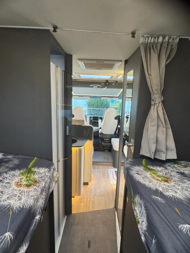 Interiér obytného auta s moderním designem, dvě postele a pohodlná řidičská sedačka. Ideální pro dobrodružství.