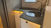 Obrázek interiéru obytného auta s moderní kuchyňkou a úložným prostorem. Designérový a praktický prostor pro cestování.