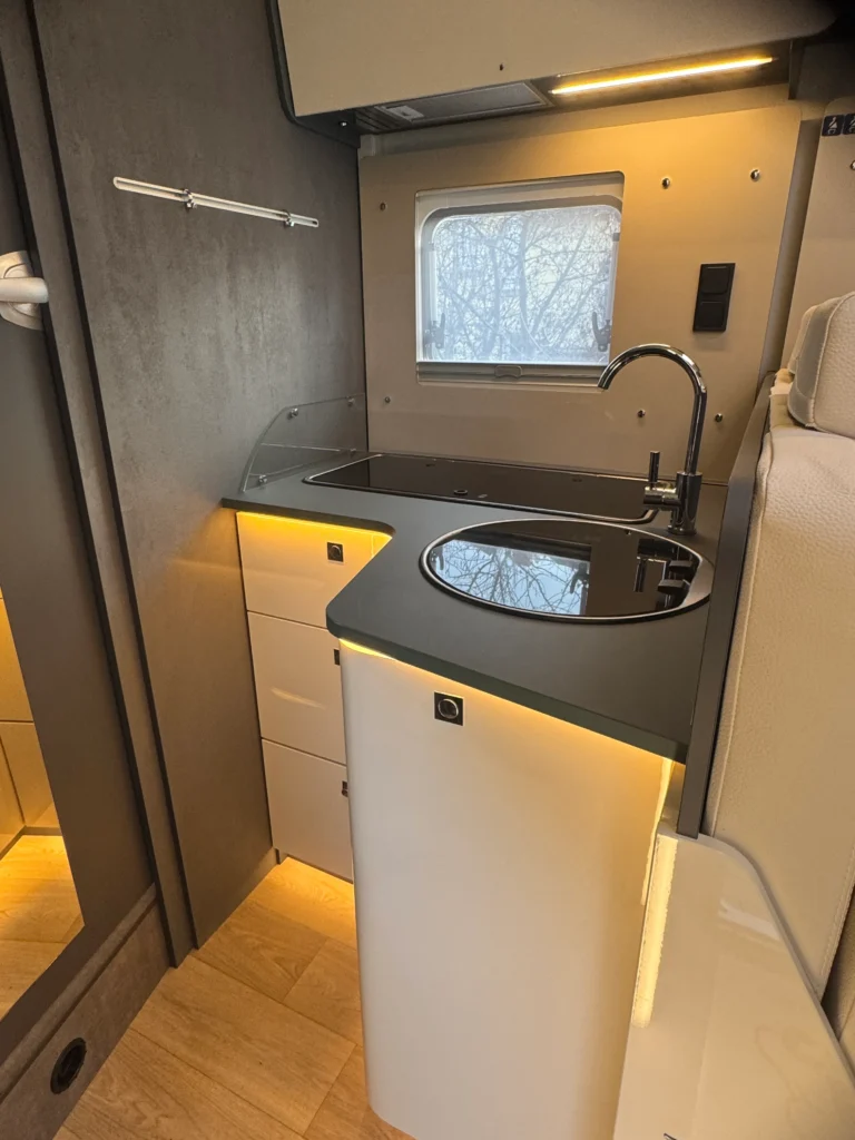 Obrázek interiéru obytného auta s moderní kuchyňkou a úložným prostorem. Designérový a praktický prostor pro cestování.