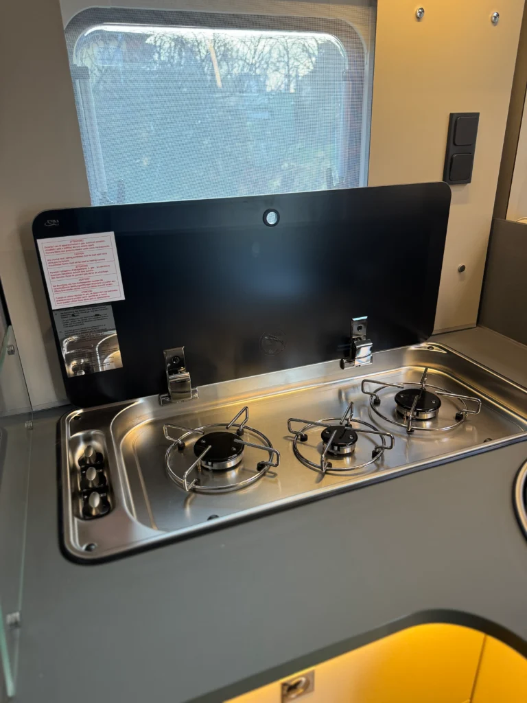 Obrázek ukazuje varnou desku v obytném voze s třemi hořáky. Elegantní design pro pohodlné vaření na cestách.