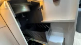 Obrázek zobrazuje část interiéru karavanu, konkrétně úložný prostor s kovovým dřezem a přihrádkou na odpadky.