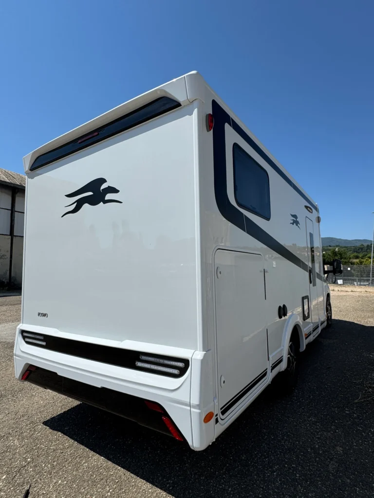 Na obrázku je bílý karavan s logem ve tvaru běžícího jelena a moderním designem.