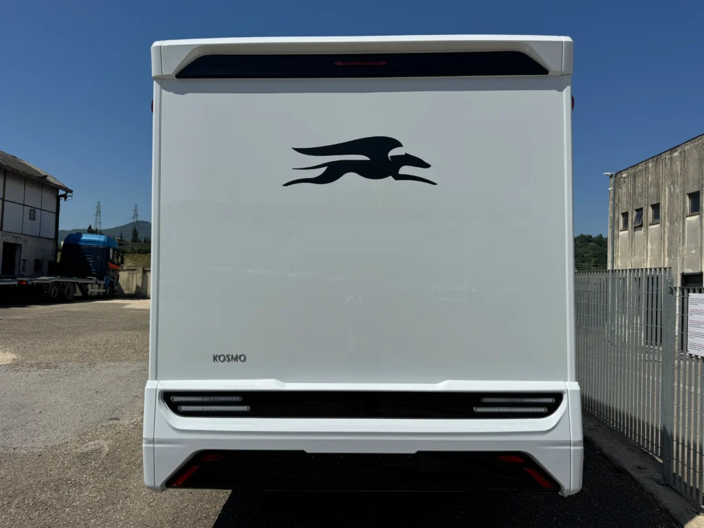 Obrázek zobrazuje bílý obytný přívěs značky Kosmo s černým logem na zadní části.