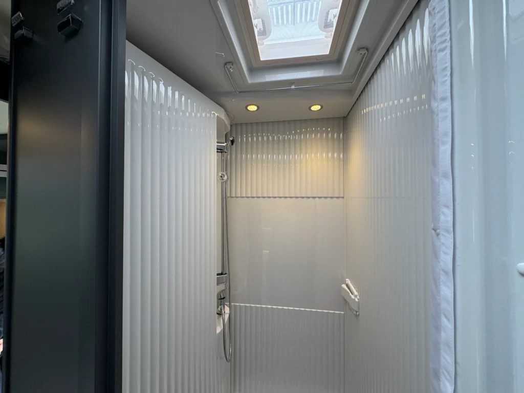 Obrázek ukazuje moderní koupelnu s sprchou, bez viditelného označení značky nebo modelu obytného vozu.