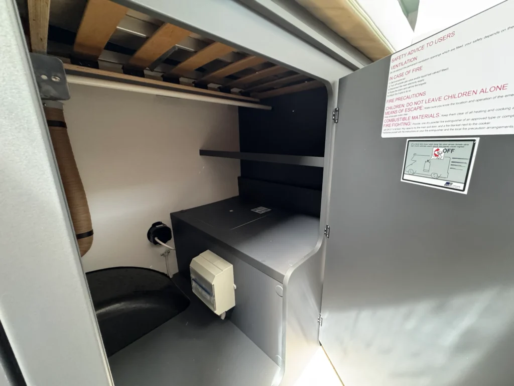 Obrázek interiéru obytného auta s úložným prostorem a bezpečnostními pokyny.