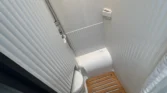 Obrázek ukazuje moderní koupelnu obytného auta s toaletu a sprchou, minimalistické bílé provedení.