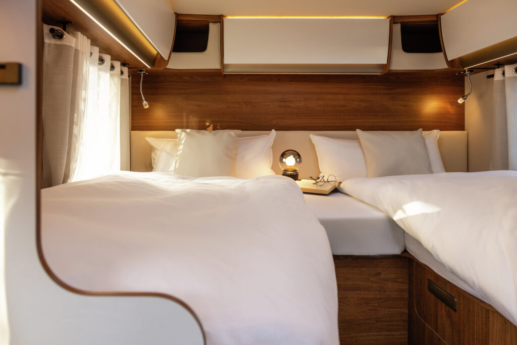 Obrázek ukazuje útulný interiér obytného vozu se dvěma postelemi a moderními doplňky.