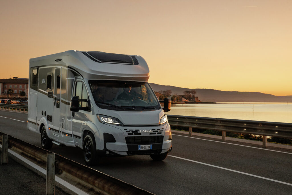Obytné auto Laika jedoucí po silnici u moře při západu slunce. Ideální pro dobrodružství!