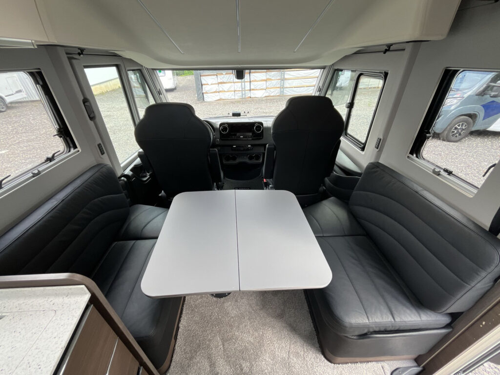 Interiér obytného auta s pohodlnými sedadly a stolem. Značka a model nejsou uvedeny.