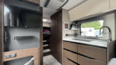 Interiér moderního obytného auta s kuchyňským koutem a pohodlnými úložnými prostory. Ideální pro cestování.