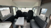 Interiér obytného auta s pohodlnými sedadly a stolem pro čtyři osoby. Značka a model nejsou uvedeny.