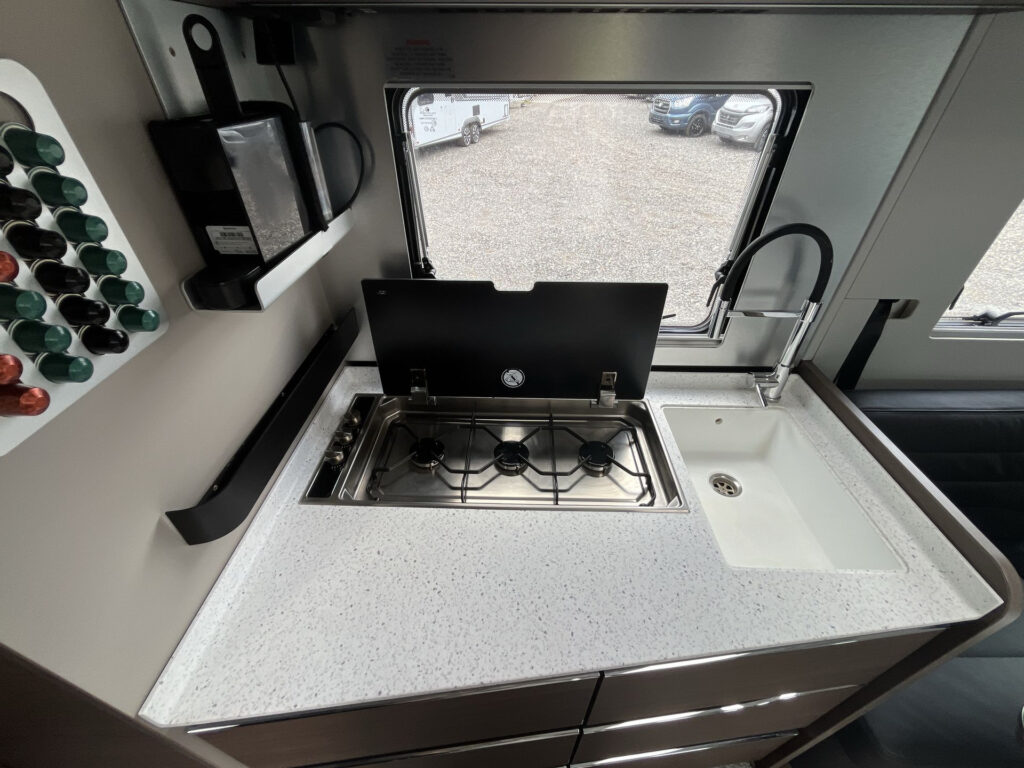 Kuchyňka obytného auta s moderním plynovým sporákem a dřezem, perfektní pro cestování a vaření na cestách.