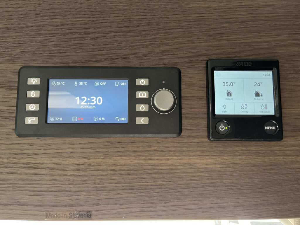 Na obrázku jsou ovládací panely pro obytné auto, které zobrazují teplotu a nastavení.