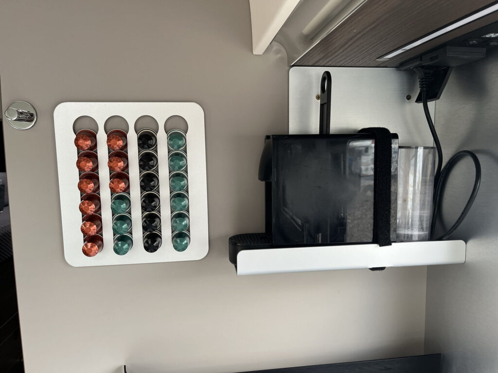 Obrázek zobrazuje coffee maker s kapslemi ve vybaveném obytném voze. Ideální pro pohodlnou přípravu kávy na cestách.