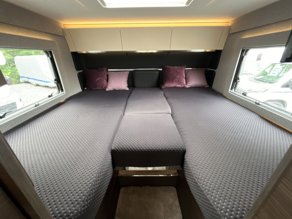 Interiér karavanu s prostornou postelí a pohodlnými polštáři. Ideální pro pohodlný spánek na cestách.