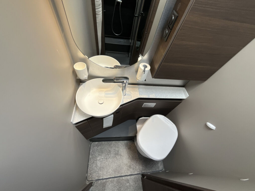 Obrázek interiéru koupelny obytného auta s moderním umyvadlem a toaletou. Elegantní design a funkčnost.