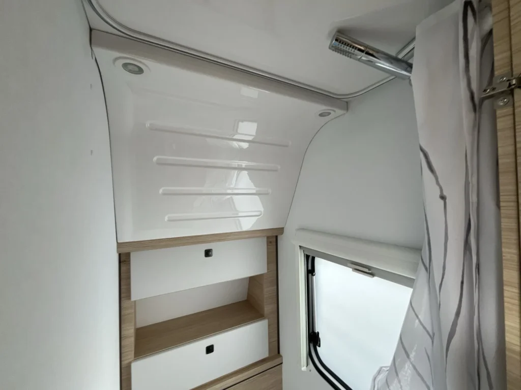 Interiér moderního karavanu s úložným prostorem a oknem pro přirozené světlo. Elegantní a praktický design.