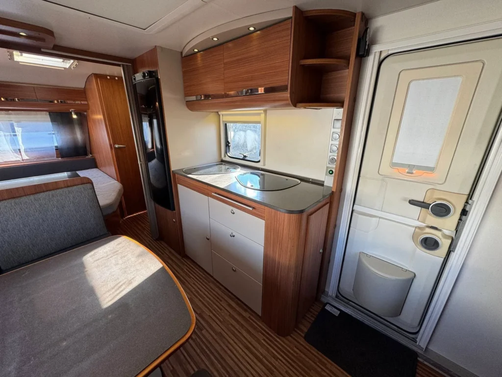 Obrázek interiéru karavanu s moderní kuchyní a posezením. Vybavení je stylové a funkcionalita na vysoké úrovni.