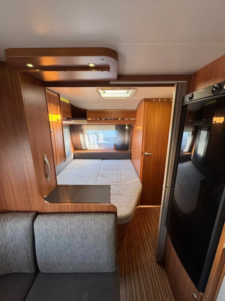 Obrázek interiéru karavanu s dřevěnými prvky a pohodlným uspořádáním pro spaní a odpočinek.