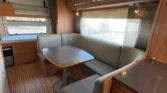 Obývací prostor karavanu s moderním designem a pohodlným posezením u stolu. Ideální pro relaxaci na cestách.