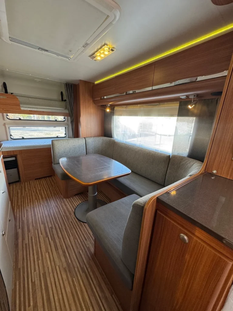 Obývací prostor karavanu s moderním designem a pohodlným posezením u stolu. Ideální pro relaxaci na cestách.