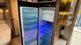 Interiér obytného auta s moderní lednicí a skříňkami, ideální pro pohodlné cestování a kempování.