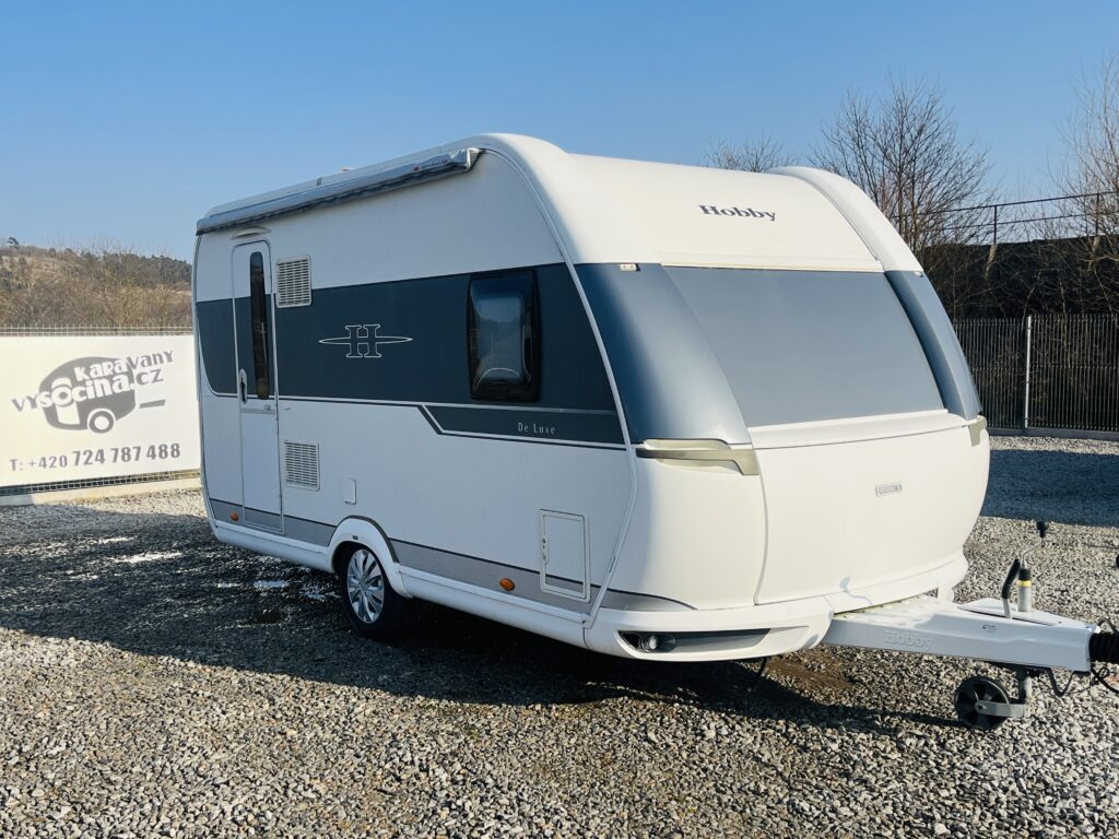 Karavan Hobby De Luxe s moderním designem a zastřešenými okny, ideální pro pohodlné cestování.