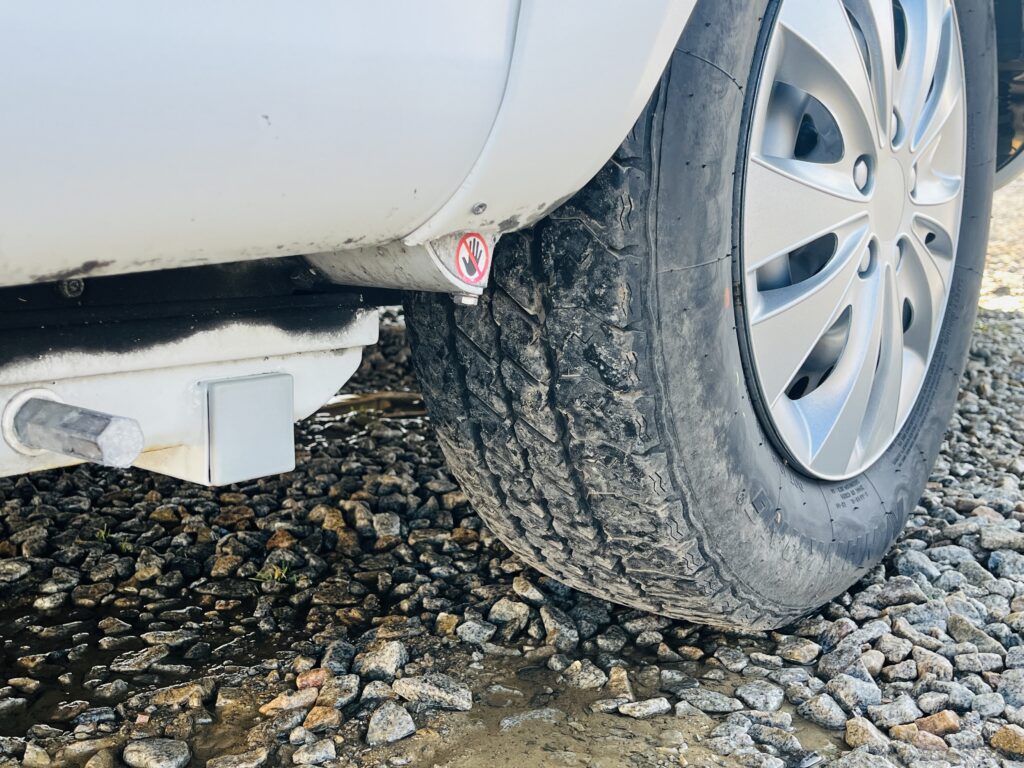 Obrázek zobrazuje kolo obytného auta s viditelným tažným zařízením. Postižené opotřebení pneumatiky je patrné.