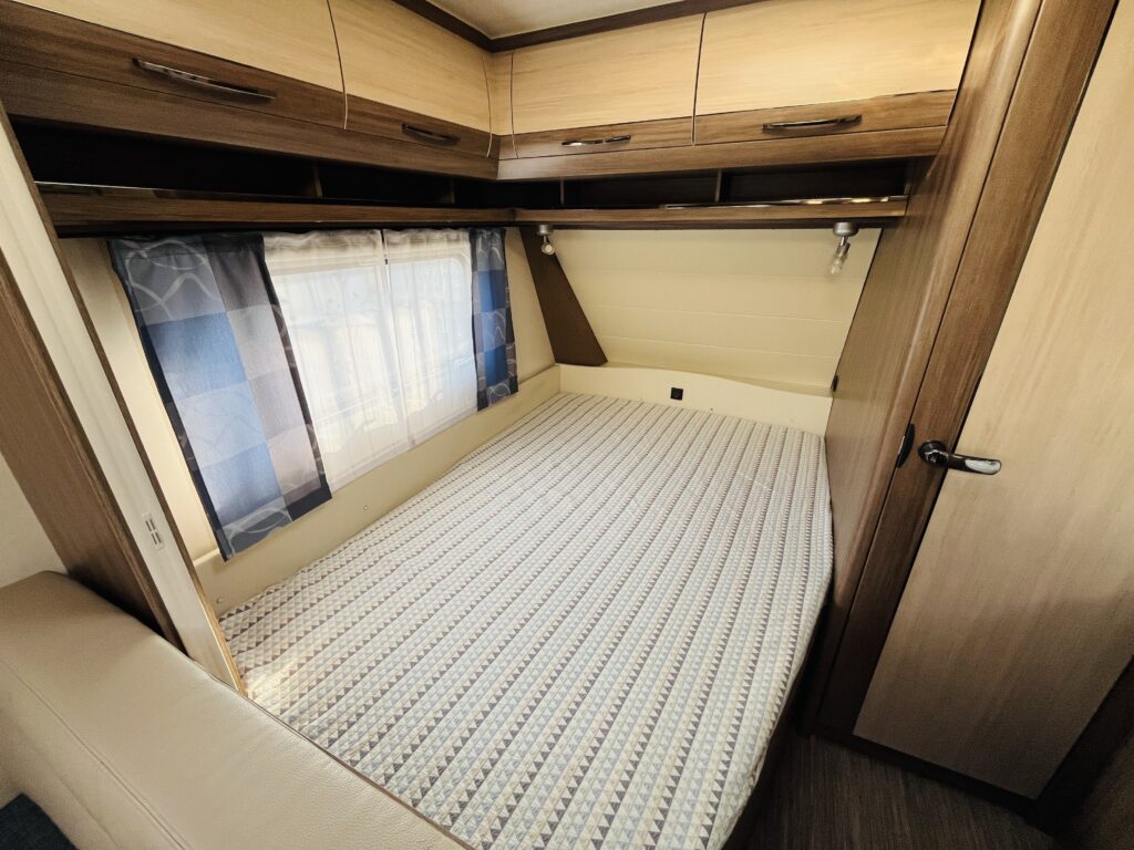 Prostorný interiér karavanu s pohodlnou postelí a úložným prostorem. Ideální pro cestování a odpočinek.