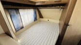 Prostorný interiér karavanu s pohodlnou postelí a úložným prostorem. Ideální pro cestování a odpočinek.