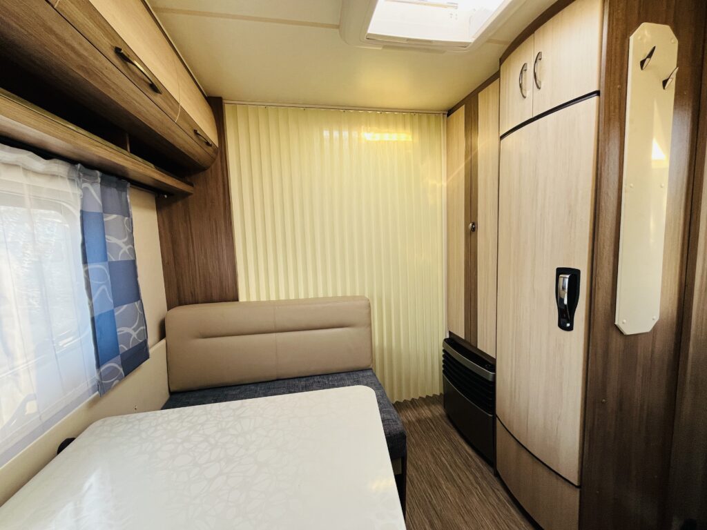 Obrázek interiéru karavanu se světlým nábytkem a pohodlným posezením. Ideální pro příjemné cestování.