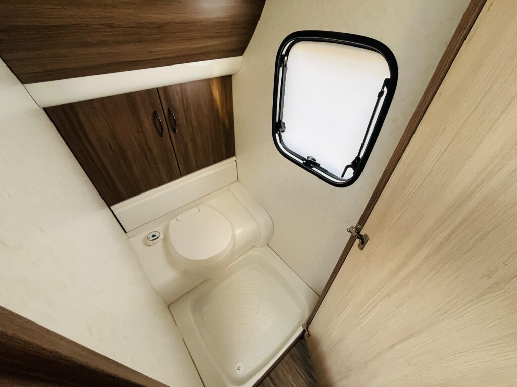 Obrázek zobrazuje koupelnu v karavanu, moderní design s toaletou a skříňkami pro úložný prostor.